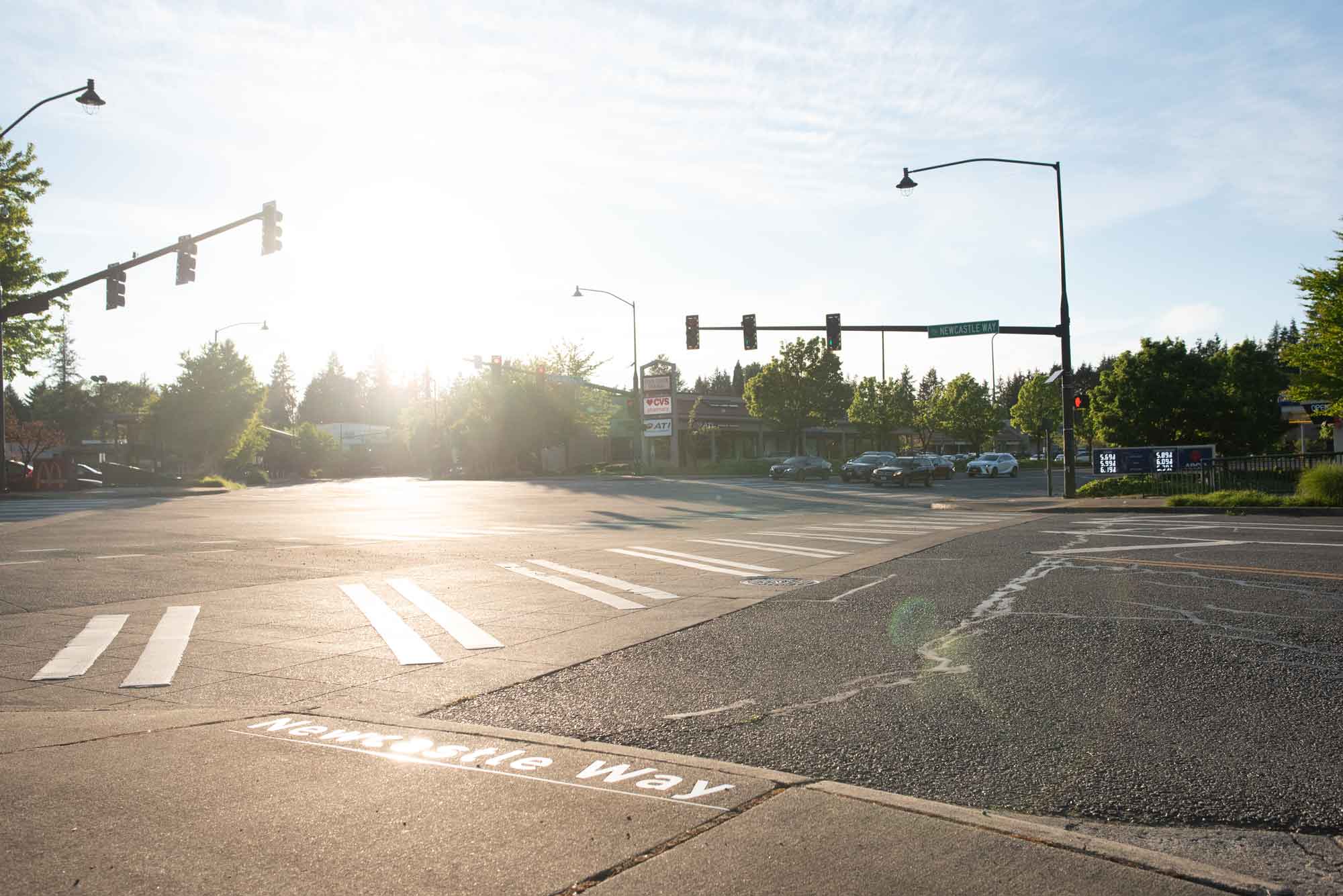 The intersection of Newcastle Way and Coal Creek Parkway in Newcastle Washington. Newcastle Way is visible on the sidewalk. Cars are stopped at a stoplight and the crosswalk is visible.